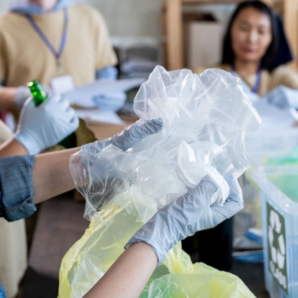 Hands of gloved volunteer sorting waste against other people