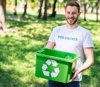 smiling volunteer holding recycling box with plastic trash