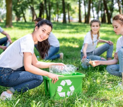 young smiling volunteers cleaning park with recycling box